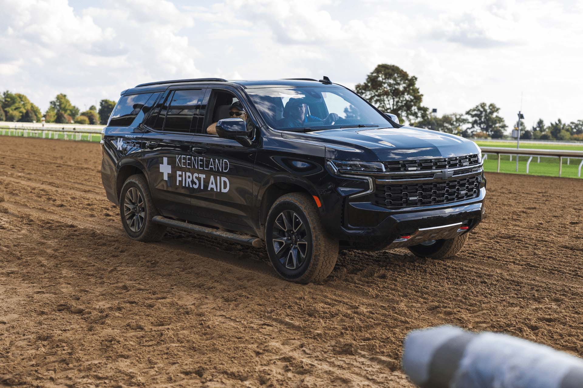 A picture of the Kneevalleytracks First Aid car on the dirt track. It is a large black Chevy SUV.